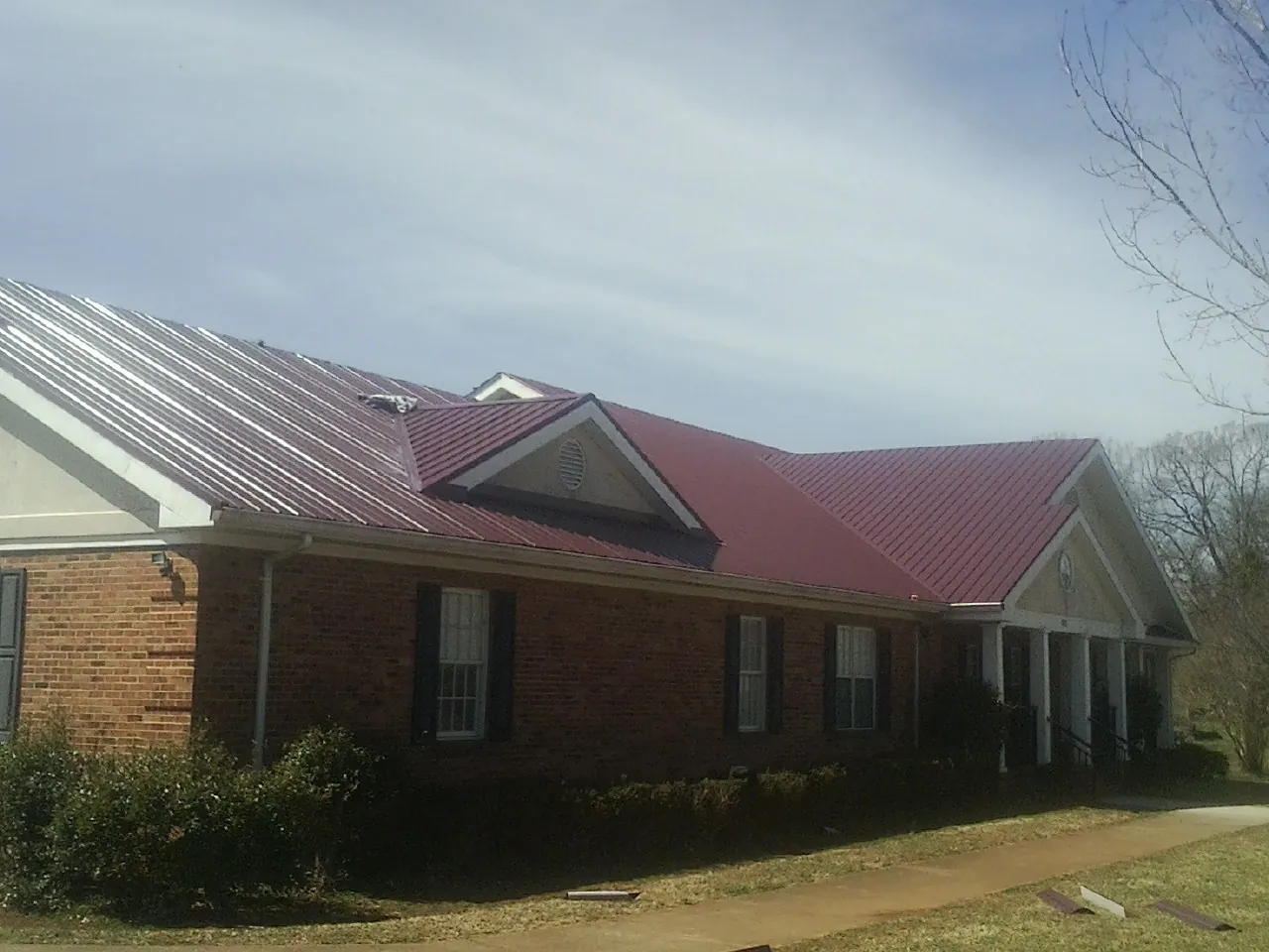 Red metal roof with gabled entries on a long brick building, from a Hail Damage Roof Repair job in Sutherland